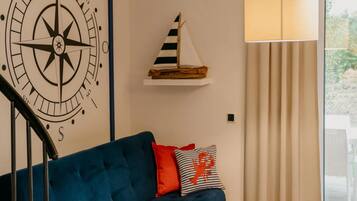 Una habitación con un sofá azul, una brújula en la pared, una decoración de velero y una lámpara.