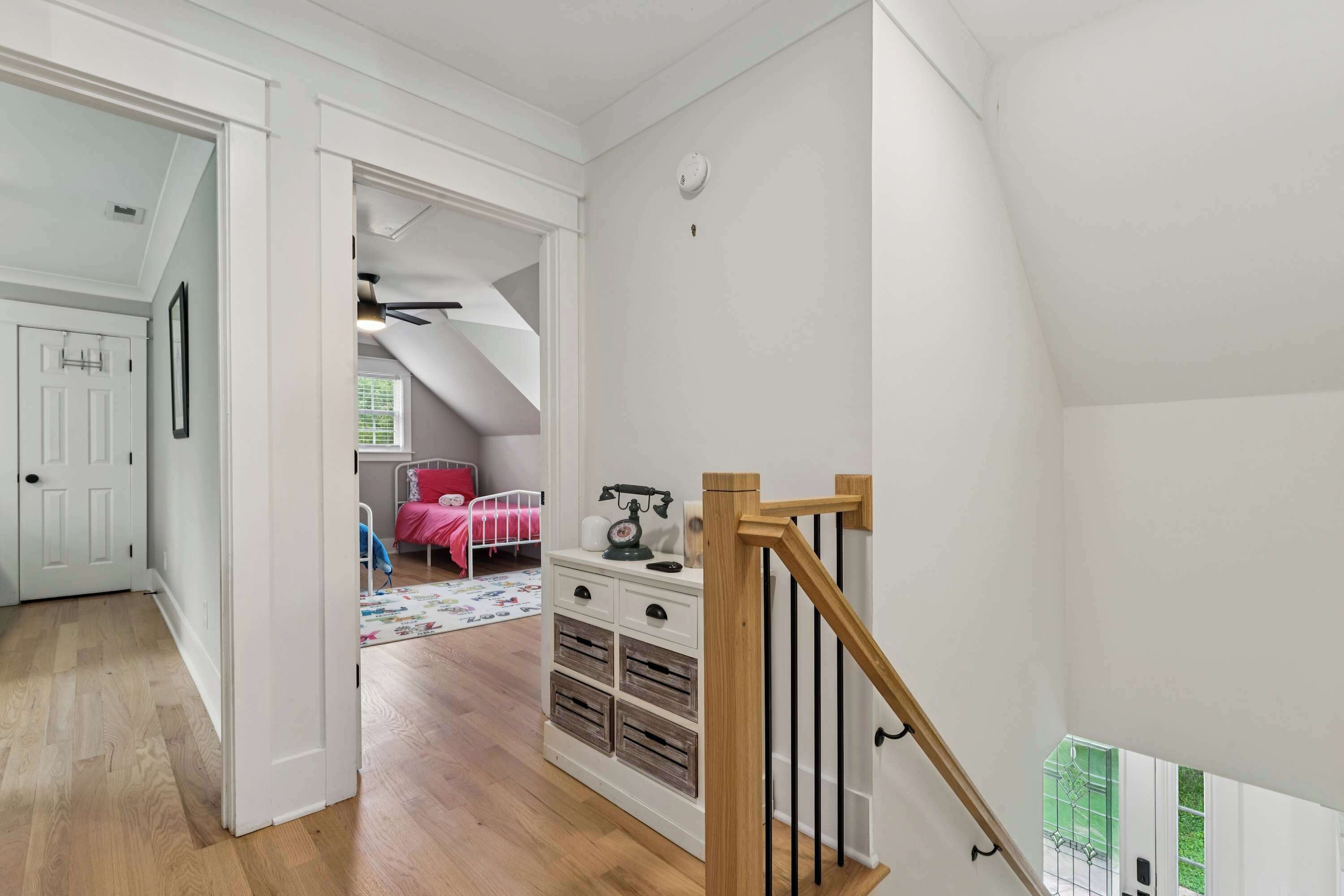 A room with a wooden staircase, a bed, a dresser, and a door leading to another room.