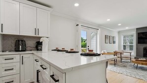 Een moderne keuken met witte kastjes, een marmeren aanrecht, een koffiezetapparaat en een eethoek met een tafel en stoelen.