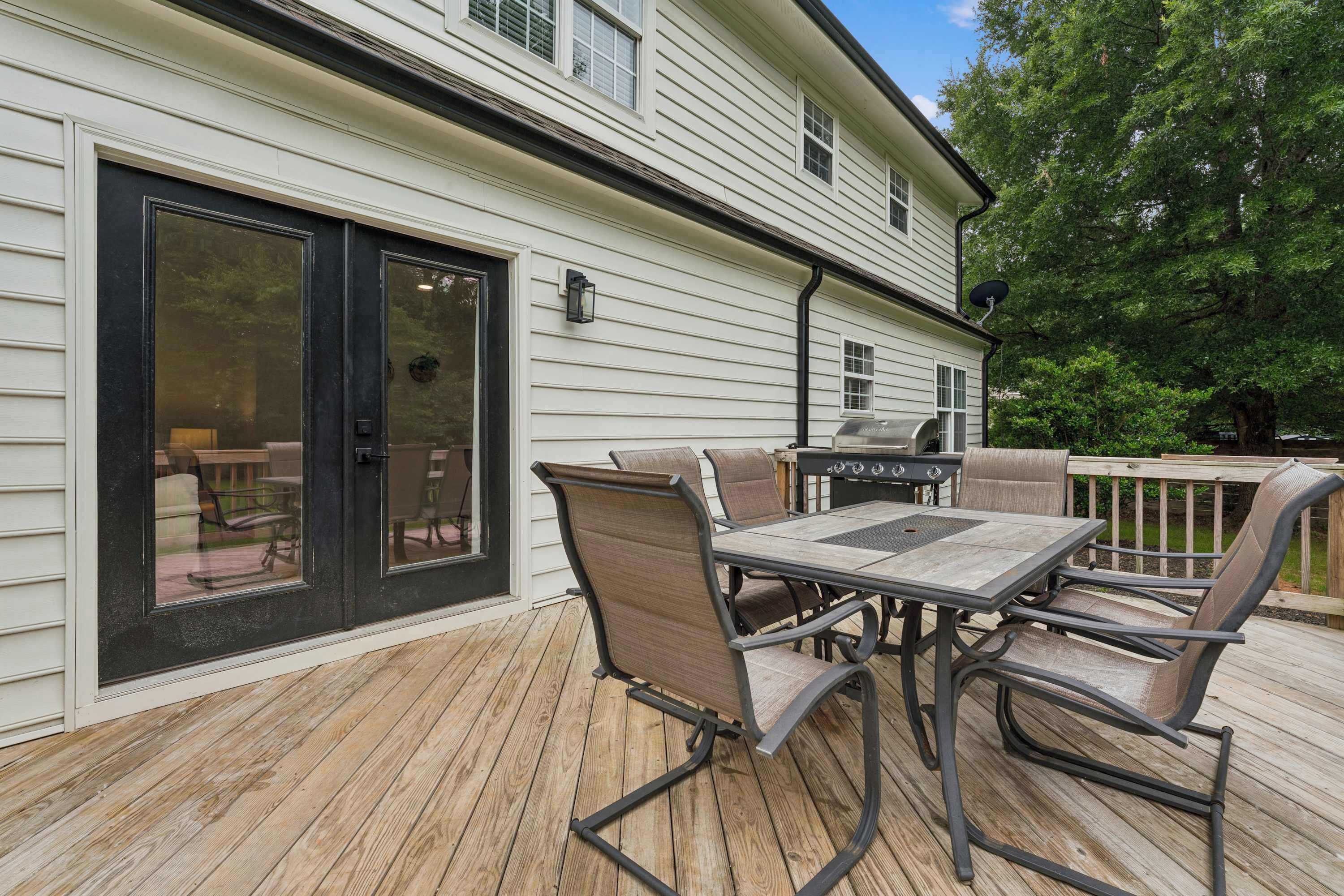 Une terrasse avec une table et des chaises, un barbecue et une porte-fenêtre coulissante.