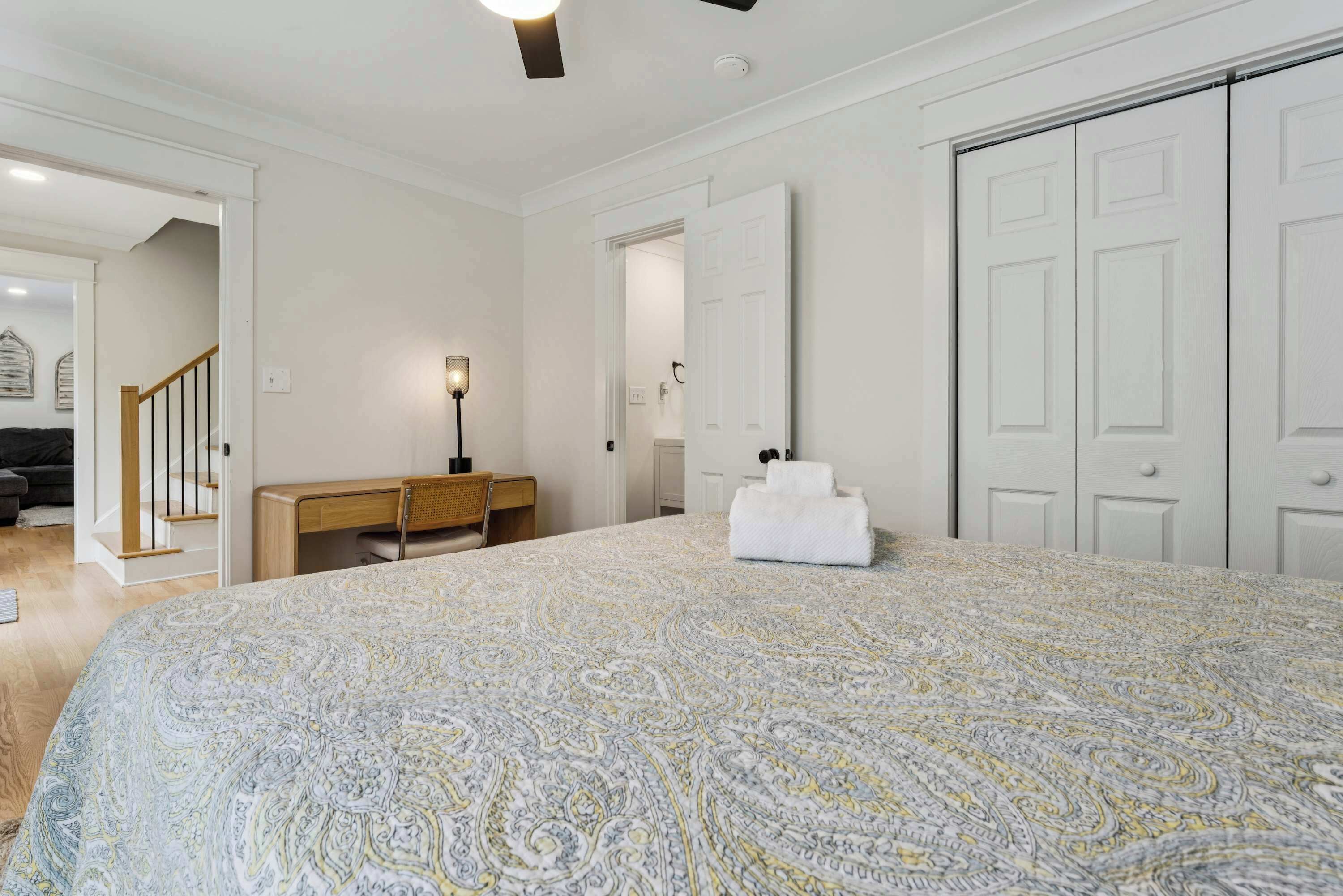 A bedroom with a large bed, a desk, a chair, a wardrobe, and a door leading to another room.