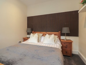 A neatly made bed with a patterned bedspread, two bedside tables with lamps, and a wooden headboard. - 10 Oak Street (Keighley)