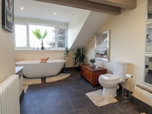 A bathroom with a freestanding bathtub, a toilet, a radiator, and a window with a view of greenery. - 10 Oak Street (Keighley)
