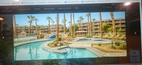 Un resort con piscina, palmeras y un edificio con balcones.
