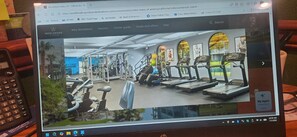 Een sportschool met fitnessapparatuur, een loopband en een persoon die een machine gebruikt.