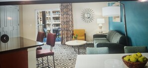 Habitación de hotel con comedor, sofá, silla, lámpara y ventana con cortinas.