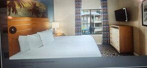 Hotelkamer met een kingsize bed, een houten hoofdeinde, een aan de muur bevestigde televisie, een raam met gordijnen en uitzicht op buiten.