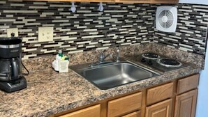 Una cocina con armarios de madera, encimera de granito, fregadero, estufa y un ventilador.
