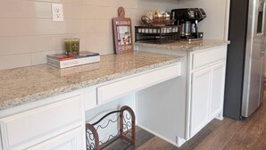A kitchen with a granite countertop, white cabinetry, a coffee maker, and a stainless steel refrigerator.