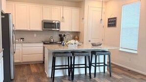 A modern kitchen with white cabinets, a stainless steel refrigerator, a microwave, and a wooden floor.