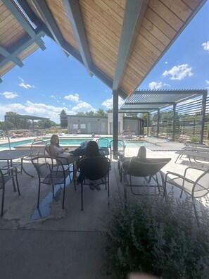 A covered outdoor area with a pool, lounge chairs, and a pergola structure.