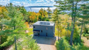 Moderni talo, jossa on kivituhkapäällysteinen ajotie, ja sen ympärillä on puita sekä näkymä järvelle.