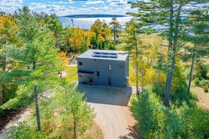 Ein modernes Haus mit Kiesweg, umgeben von Bäumen und Seeblick.