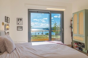 Ein Schlafzimmer mit einer großen Glasschiebetür, die auf einen Balkon mit Blick auf einen See und Bäume führt.