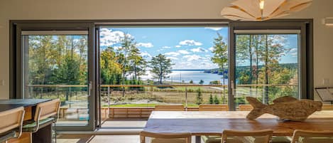 A modern dining area with a large table and chairs, a wooden fish sculpture, and a view of a lake through large windows.