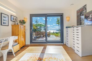 Ein modernes Interieur mit einer Schiebeglasdoor zum Außenbereich, einem Holzkasten, einem weißen Schreibtisch und einem weißen Stauraum.