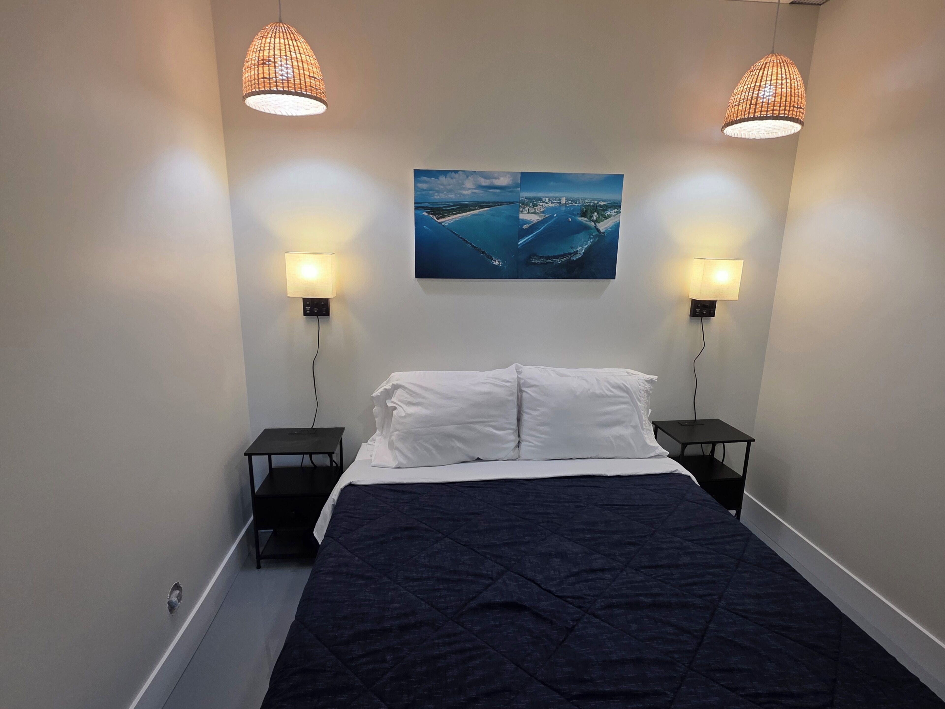 A bedroom with a bed, two bedside tables, two wall-mounted lamps, and a framed picture on the wall.