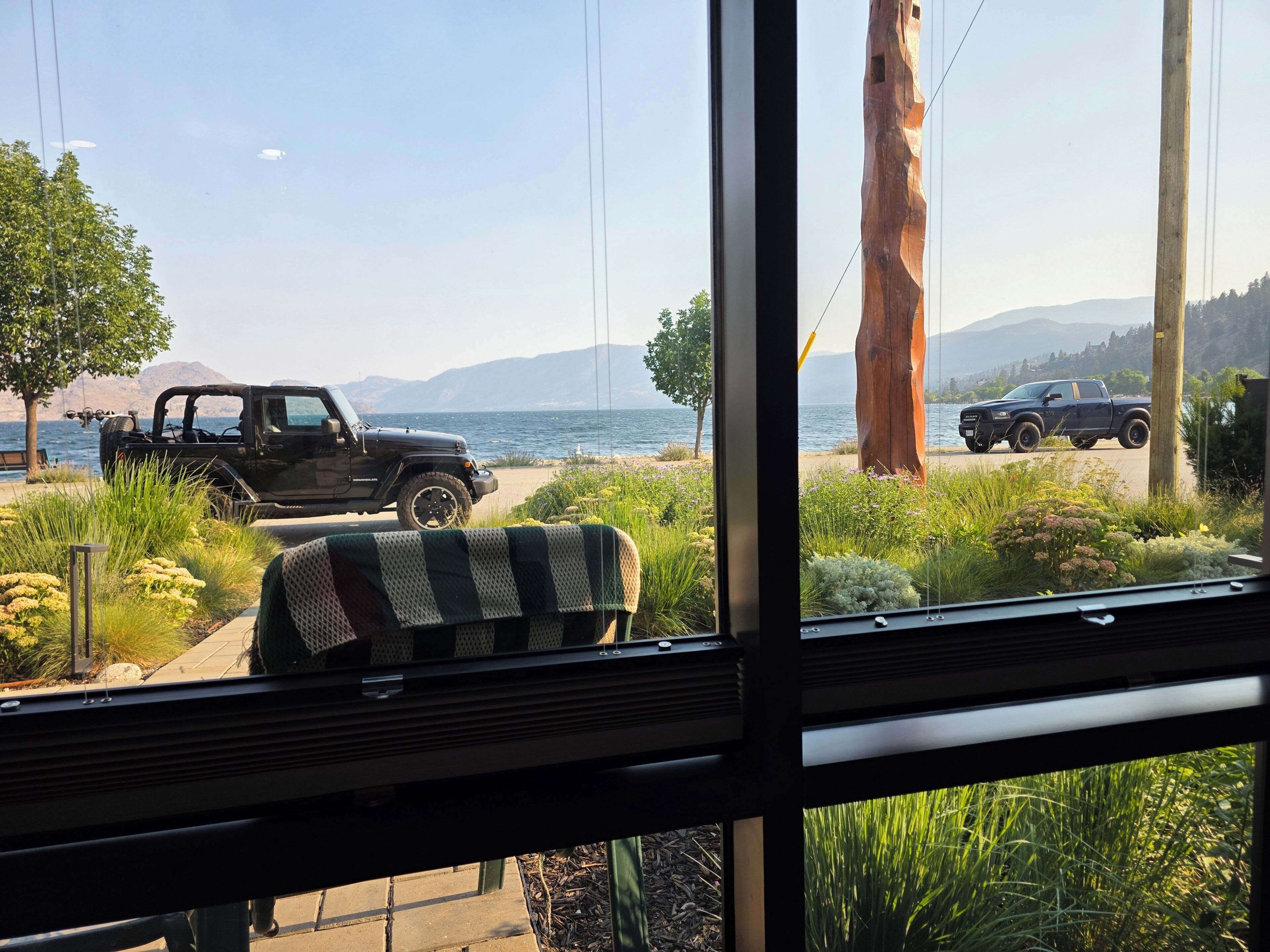 A view from inside a room with a window overlooking a beach with parked vehicles and a large tree.