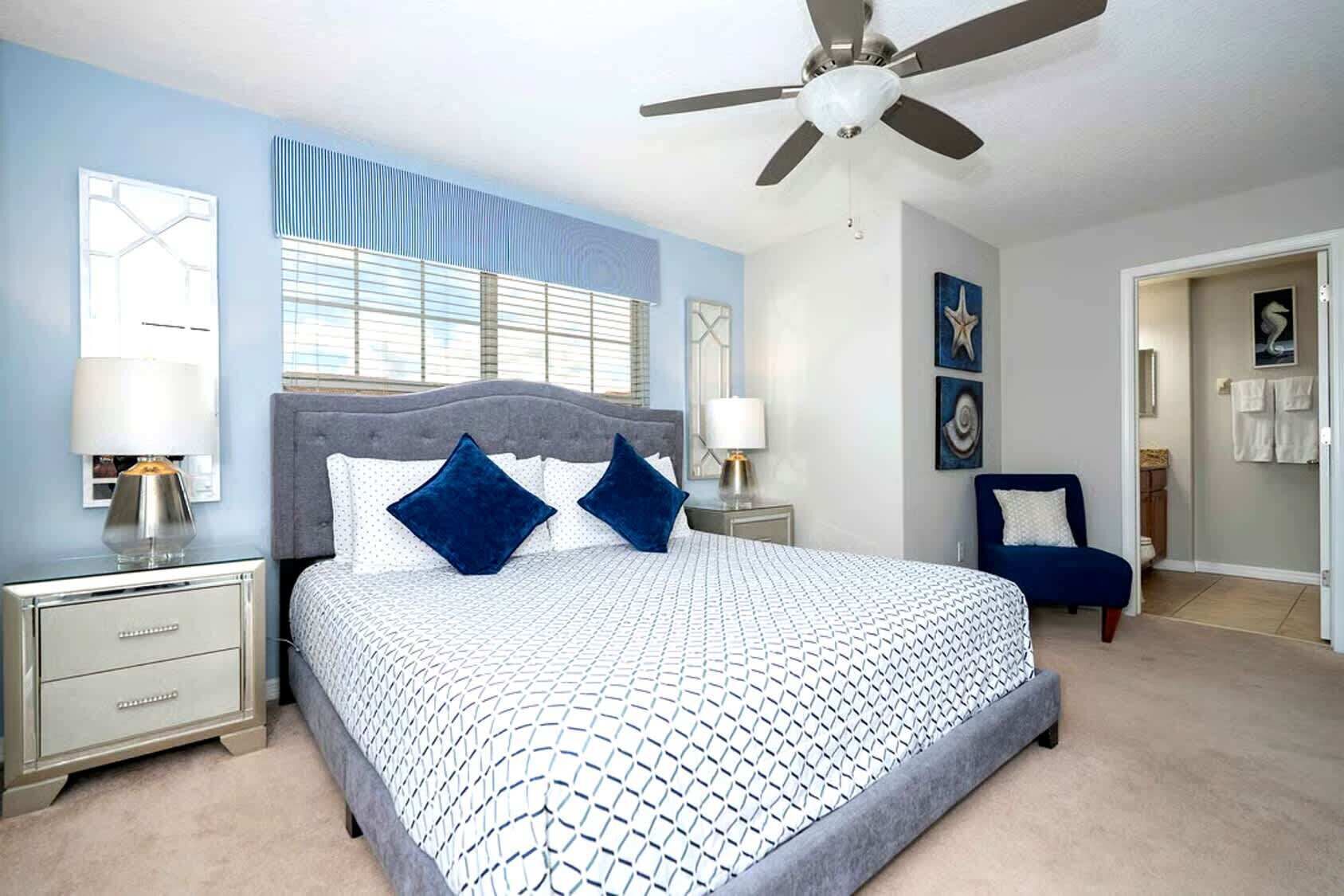 A bedroom with a bed, nightstands, a chair, a ceiling fan, and artwork on the walls.