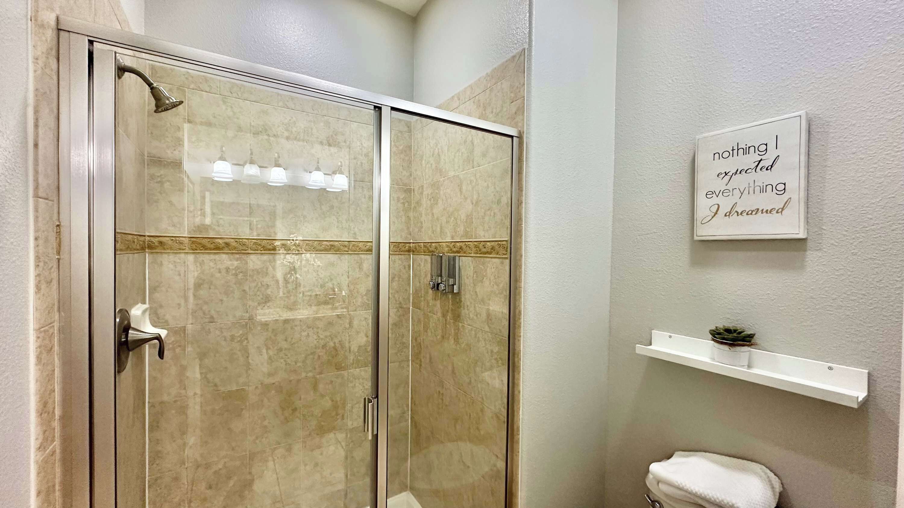 A glass-enclosed shower with a handheld showerhead and a wall-mounted light fixture.