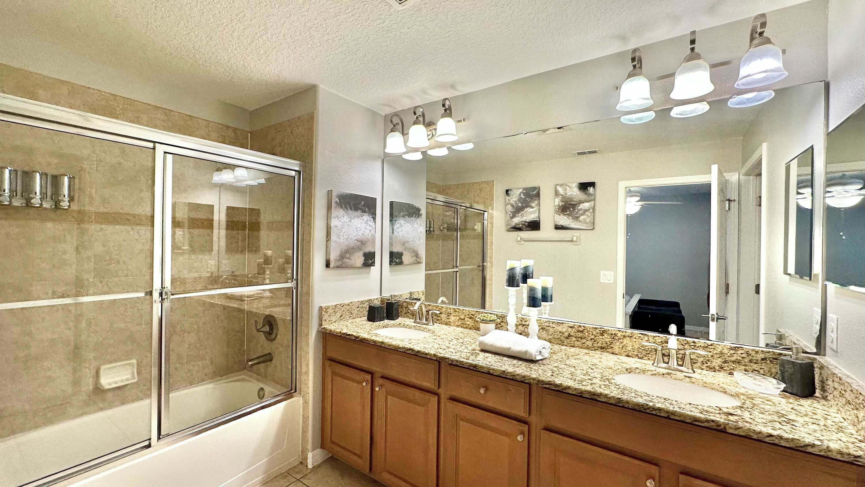 A bathroom with a glass shower enclosure, a double sink vanity, and a large mirror.