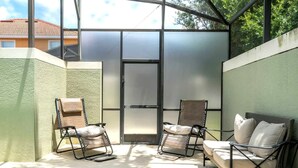 A sunlit patio with a pool, two chairs, a sofa, and a sliding glass door. - Golden Hours at Paradise Palms (Kissimmee)