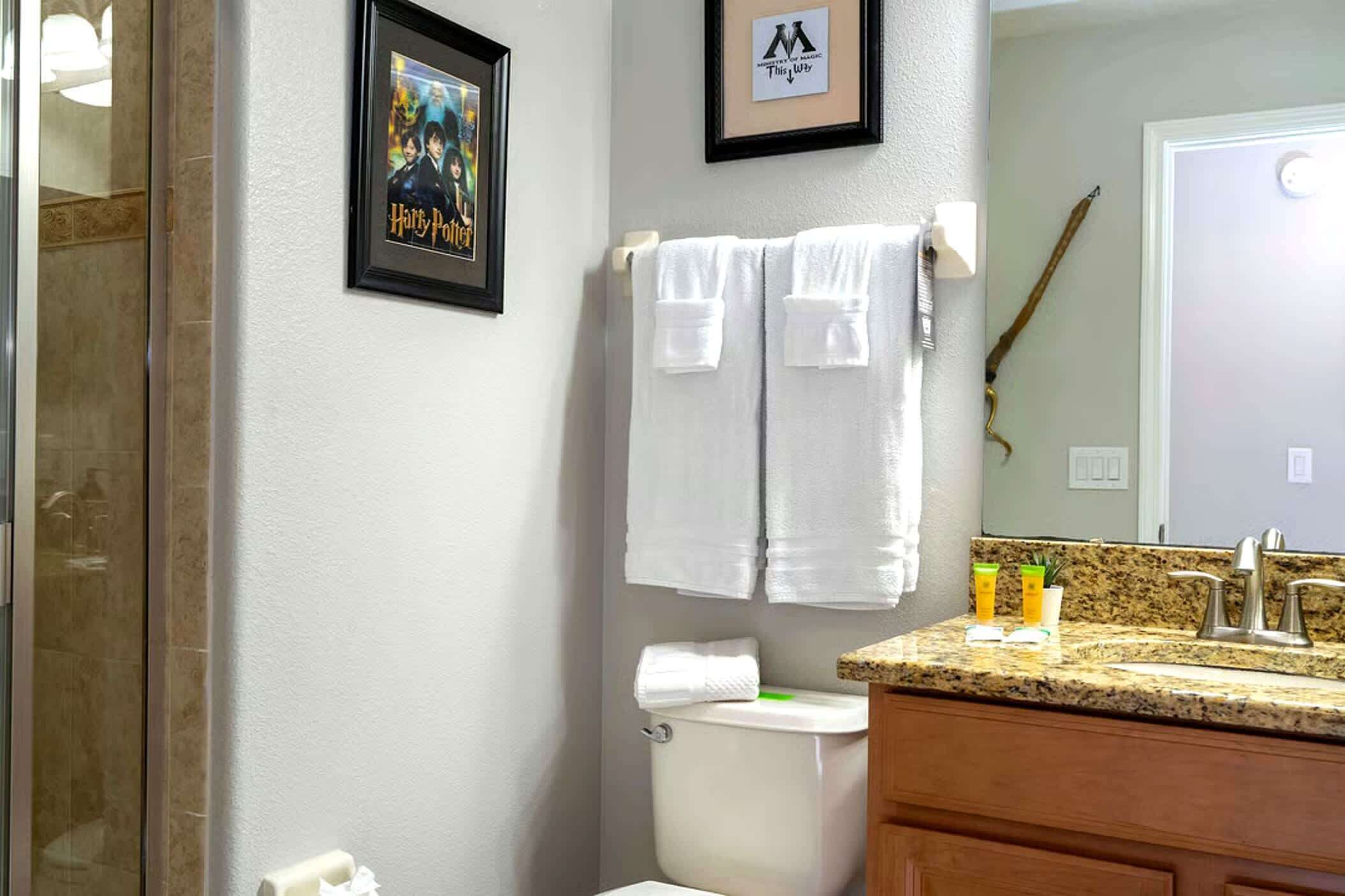 Casa de banho com um quadro do poster de Harry Potter, sanita, lavatório com artigos de higiene e espelho.