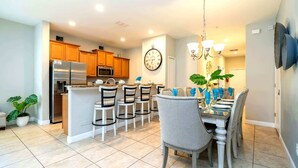 A modern kitchen with a central island, wooden cabinets, and a dining area with a chandelier. - Golden Hours at Paradise Palms (Kissimmee)