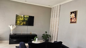 Una sala de estar moderna con un sofá negro, un televisor montado en la pared, una mesita blanca y una planta en maceta.
