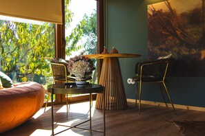 A room with a large window, a round table with chairs, a sofa, and a painting on the wall. - Country House 'D’Olívia Lovely Homes - Conceição' with Shared Garden, Wi-Fi & Air Conditioning (Cela)
