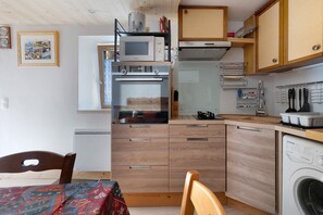 Eine kompakte Küche mit Mikrowelle, Backofen und Geschirrspüler. Ein Esstisch mit Stühlen und einer gemusterten Tischdecke steht bereit.