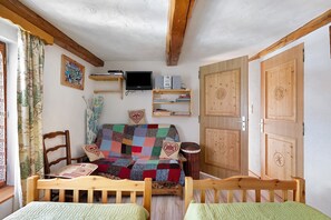 Een gezellige kamer met een houten bed, een bank met een lappendeken, een televisie en een boekenplank.