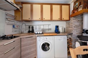 A compact kitchen with wooden cabinets, a built-in washing machine, and a coffee maker. - Le Planay. Chambéranger – Apartment in a Traditional Savoyard Village (Planay)
