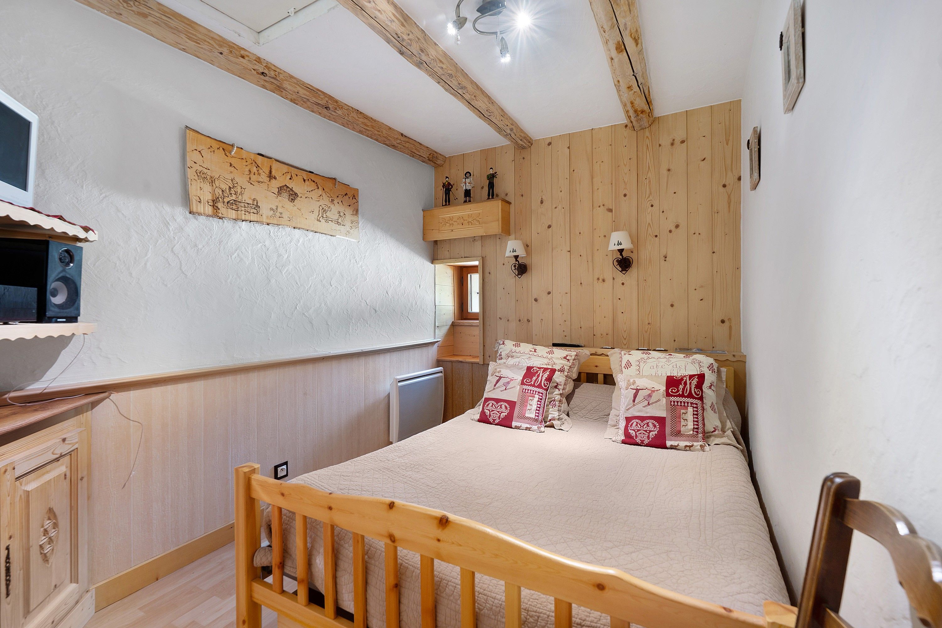 Een slaapkamer met een houten bed, een dressoir, een wandplank met beeldjes en een plafondventilator.