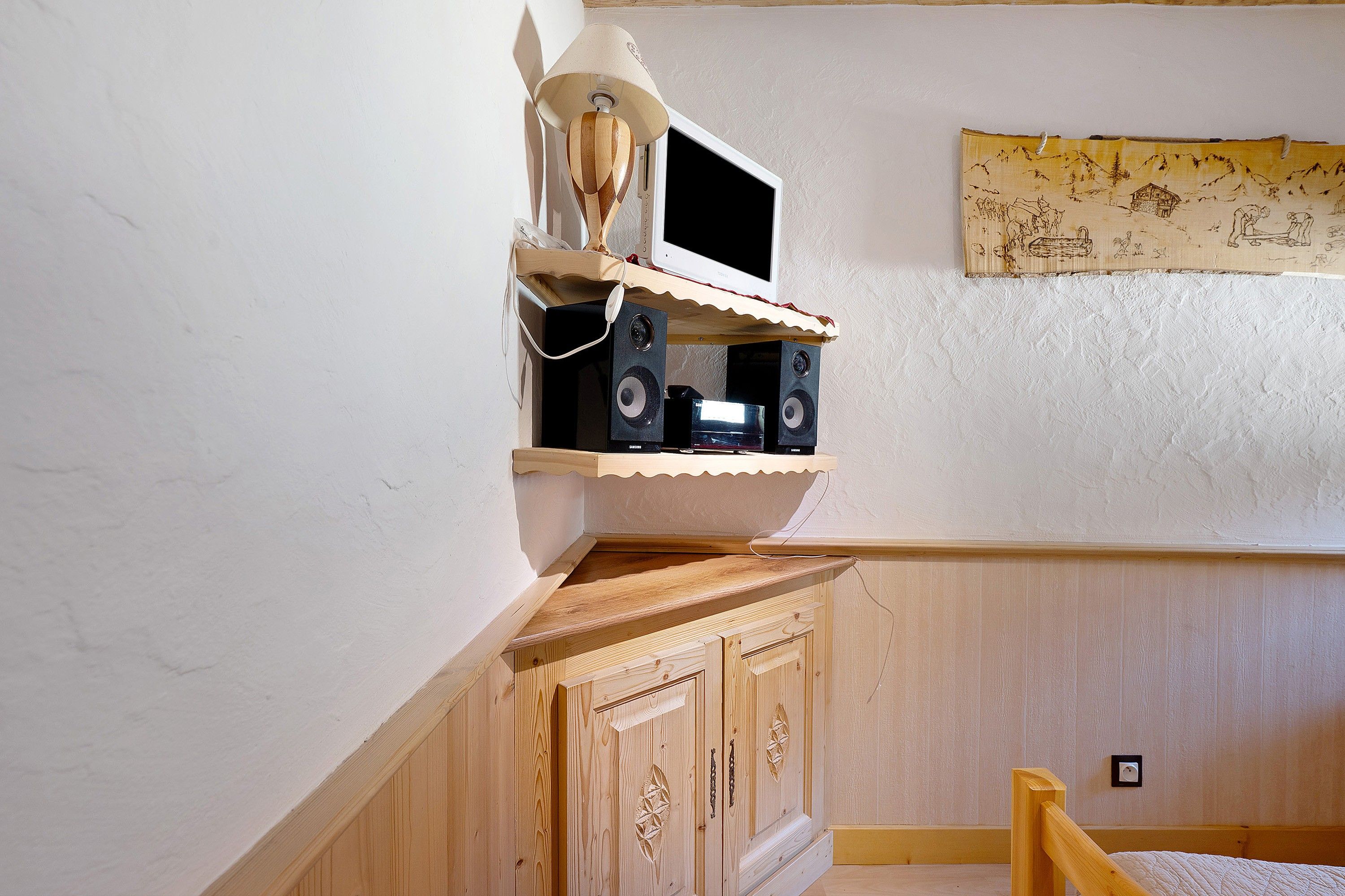 A room with a wooden cabinet, a mounted television, and a wall with a decorative tapestry.