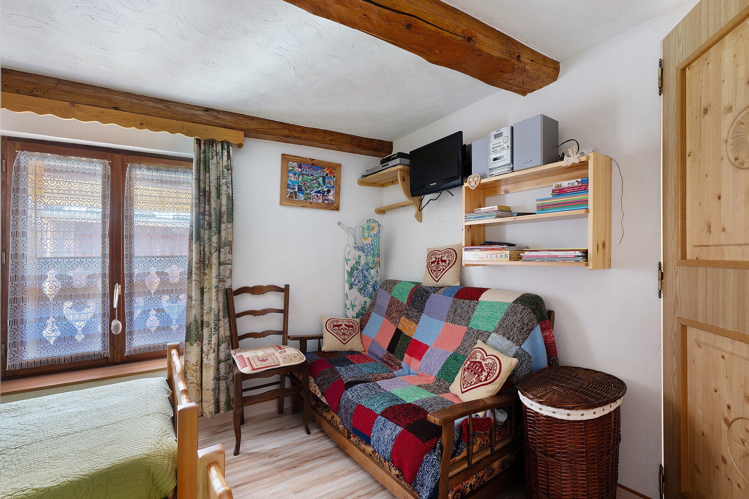 Ein gemütliches Wohnzimmer mit einer Holzcouch, einer gemusterten Decke, einem Holzstuhl, einem Fernseher und einem Bücherregal.