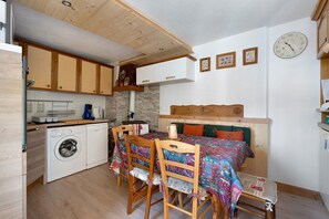 Een kleine keuken met een wasmachine, houten kastjes en een eethoek met een tafel en stoelen.