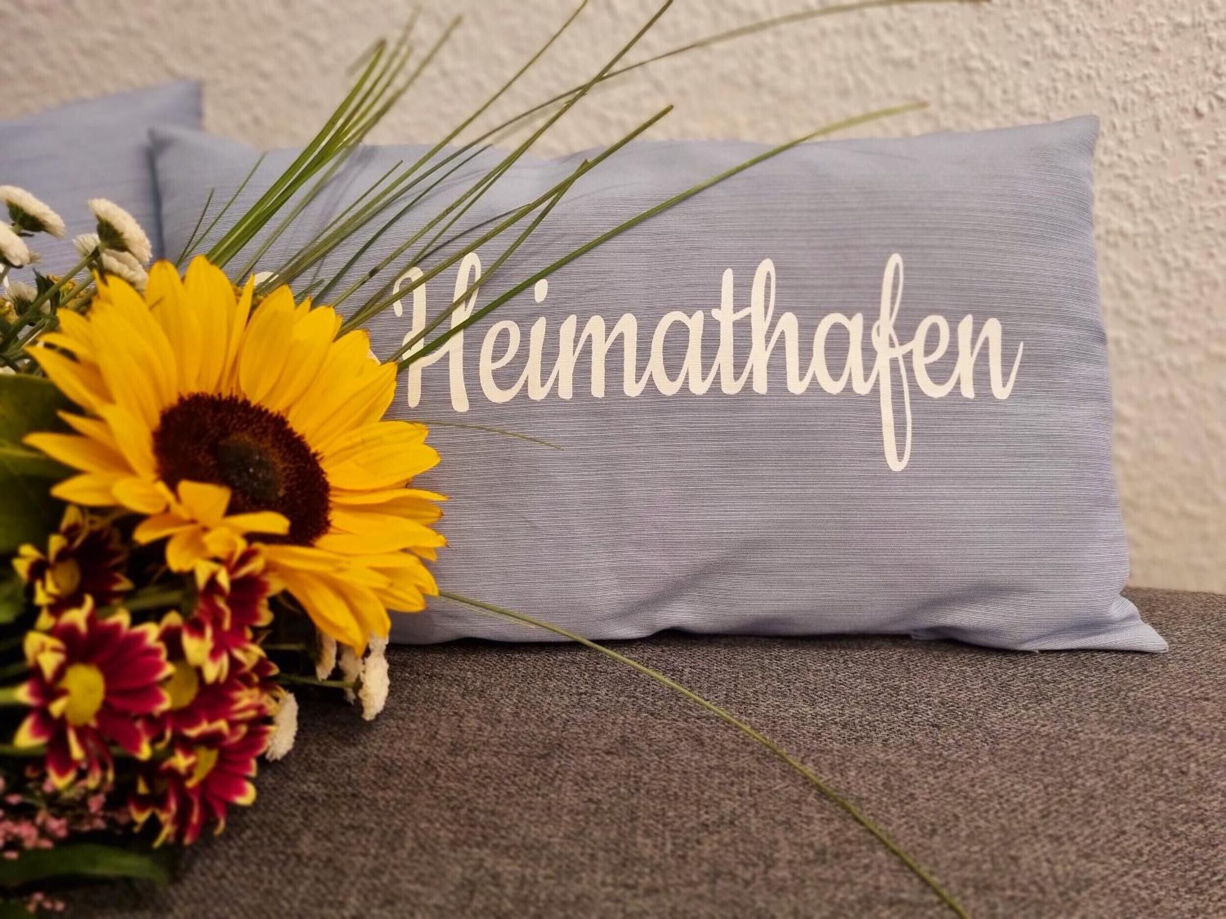 A pillow with the name 'Heimathafen' and a bouquet of flowers.
