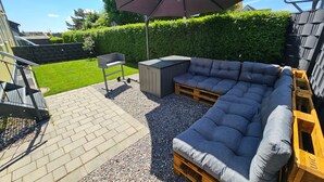 Un patio con una panca di legno, un barbecue e un ombrellone grande.