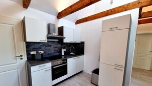 Una cucina compatta con mobili bianchi, un piano di lavoro nero, forno integrato e frigorifero in acciaio inossidabile.