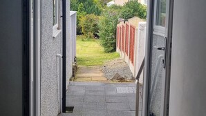 A narrow pathway leading to a garden with a red fence, a small pond, and a house in the background. - Ehen Cottage (Cleator Moor)