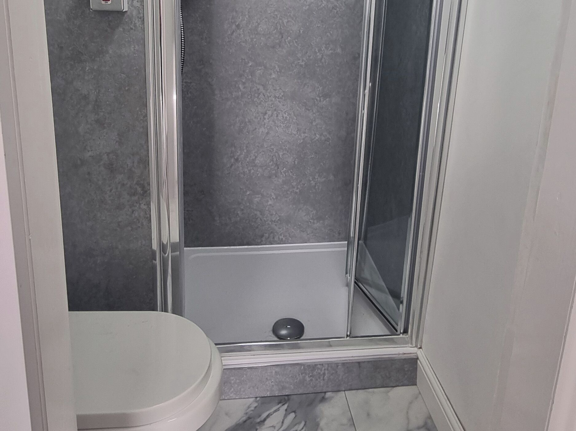 Et badeværelse med bruser, toilet og marmorgulv.