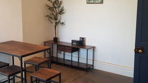 Una habitación con una mesa de madera, bancos, una planta en maceta, un pequeño armario y un cuadro en la pared.