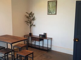 A room with a wooden table, benches, a potted plant, a small cabinet, and a framed picture on the wall.
