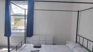 Una cama con dosel con sábanas blancas, un radiador y un ventanal con cortinas azules.