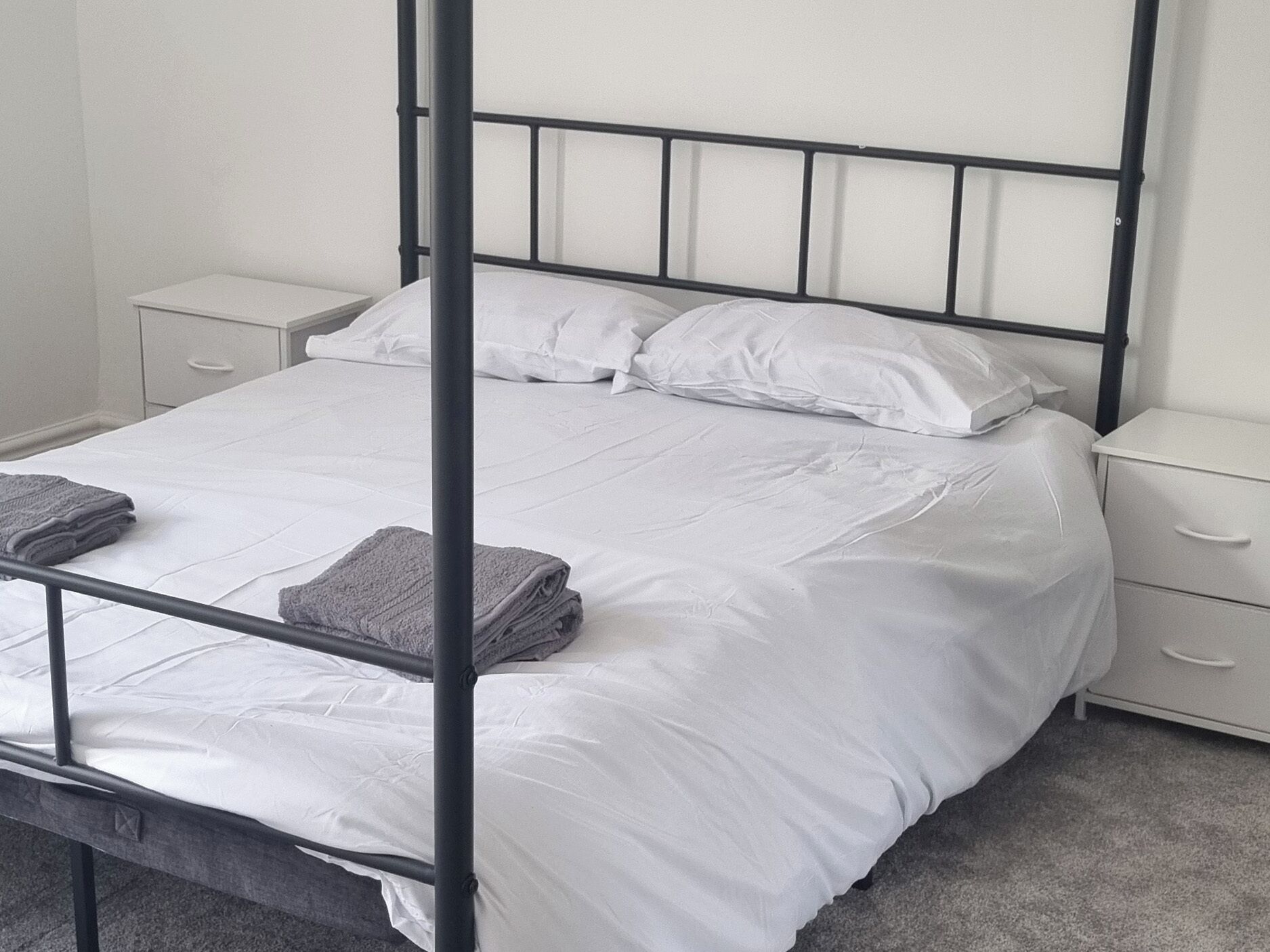 Un lit simple avec un cadre en métal, une literie blanche et deux tables de chevet avec des tiroirs.