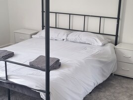 Una cama individual con estructura metálica, ropa de cama blanca y dos mesitas de noche con cajones.