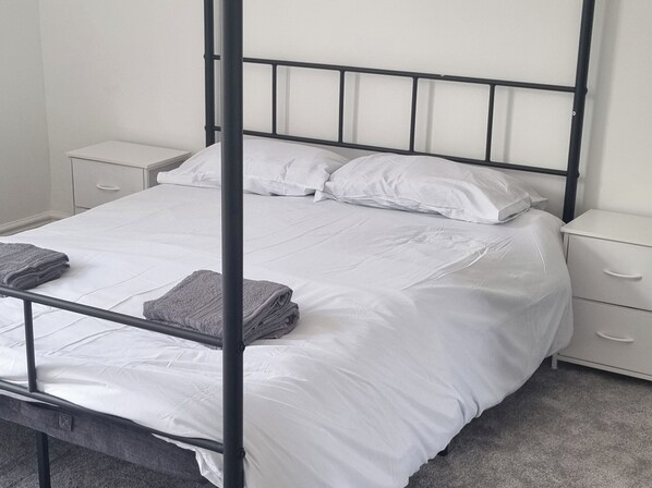 Una cama individual con estructura metálica, ropa de cama blanca y dos mesitas de noche con cajones.