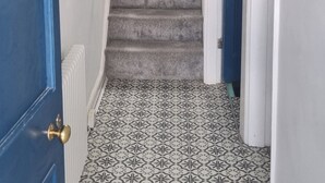 Un pasillo estrecho con una escalera alfombrada, baldosas de suelo estampadas y una puerta azul con picaporte de latón.