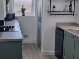 Una cocina con microondas, estufa, lavaplatos y una estantería con una botella y una planta.
